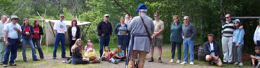 An interpreter in voyageur dress prepares to fire a black powder musket as visitors listen.