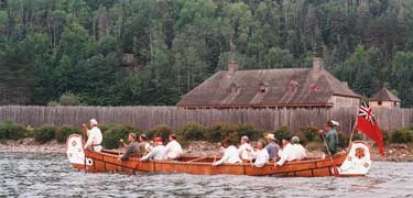A 40' Montreal canoe being paddled by 12 voyageurs approaches the depot at Grand Portage.