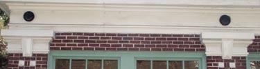 detail of upper part of windows with multi-panes inside green painted trim against red brick of the building with two black patera above