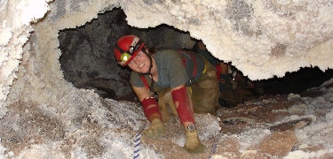 A caver crawls under a frostwork rim (NPS Photo)