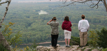 Visitors stand on top of a high bluff overlooking the forest and river below.