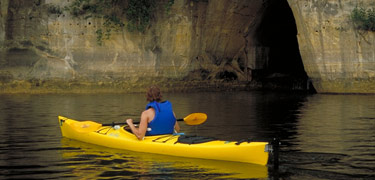 Kayaker in a bright yellow kayak on the Mississippi River near a vertical cliff.