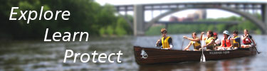 Youth enjoying a canoe ride on the Mississippi River. A large bridge spans the river between wooded shorelines.