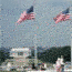 Visitors sit underneath flags on the National Mall with the Lincoln Memorial in the background.