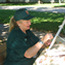 A woman in a green shirt weaving on a small loom outdoors.