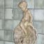 portion of ceramic fountain, a light gray colored cherub sitting on an open-mouthed fish, with blue square tiles behind
