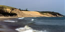 A view looking across water of a large sand dune mostly bare with some grass