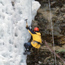 A winter visitor scales a column of ice with ropes and ice pick.