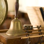An old fashioned bell, globe, books, and pencils on a teachers desk.