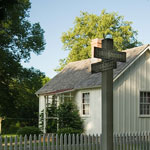 A white cottage stands at an intersection marked by a wooden sign post.