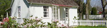 A small white cottage with pink flowers blooming in front.
