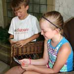 Young white boy on left, young white girl sitting in right foreground, both holding and looking at trading cards