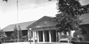 Black and white photo of the Government Free Bathhouse with a ranger walking on the sidewalk in front. Black and white photo of the Government Free Bathhouse with a ranger walking on the sidewalk in front.