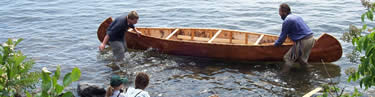 Two canoemen, knee deep in water, wet their birchbark canoe in Lake Superior before going for a paddle.
