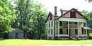 log cabin and a three story house with trees behind and grass in front log cabin and a three story house with trees behind and grass in front