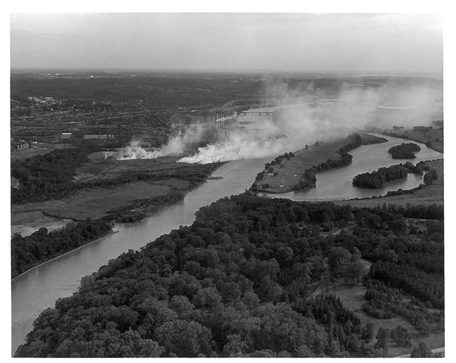 An aerial black and white photo shows smoke wafting from the landfill across the Anacostia River and over the Langston golf course.