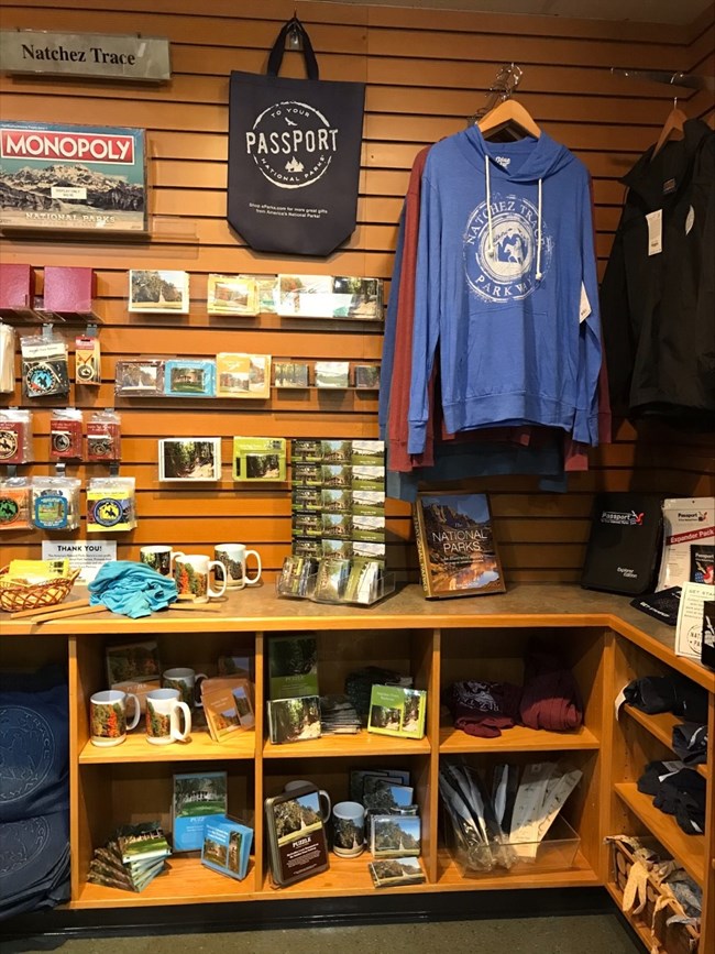 A portion of ta store filled with items sporting the Natchez Trace Parkway logo, including a blue hoodie, cups, stickers and refrigerator magnets.