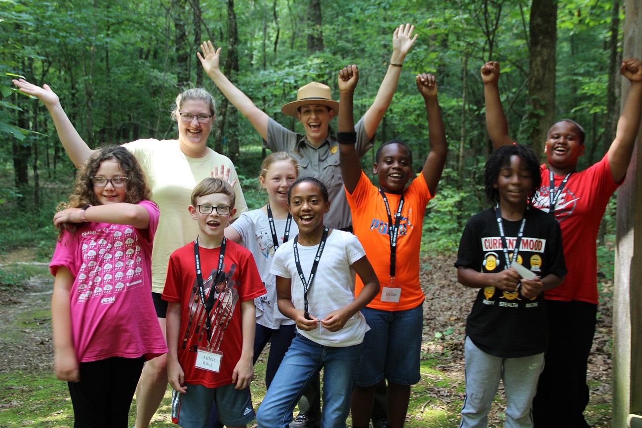 A park ranger, teacher, and students rejoicing with arms in the air.