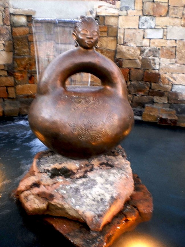 a sculpture of a closed pot with a round bottom, arched handle and head on the top.