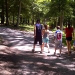 four youth walking on a wide natural surface path toward a green forest four youth walking on a wide natural surface path toward a green forest
