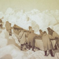 Men push a canoe over the snow and ice.
