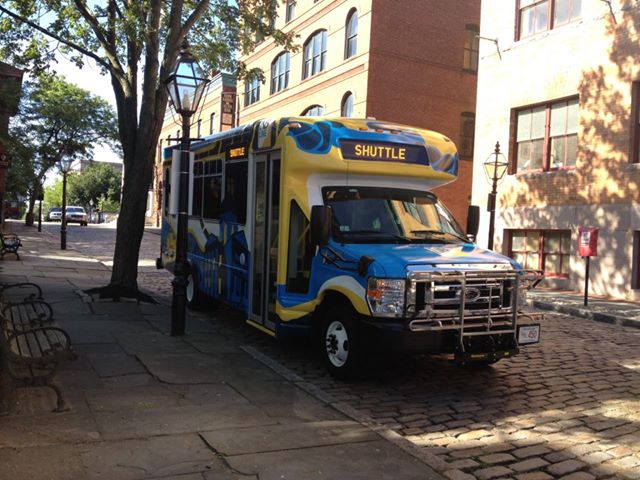 NB Line shuttle covered in blue and yellow graphics parked on second street.