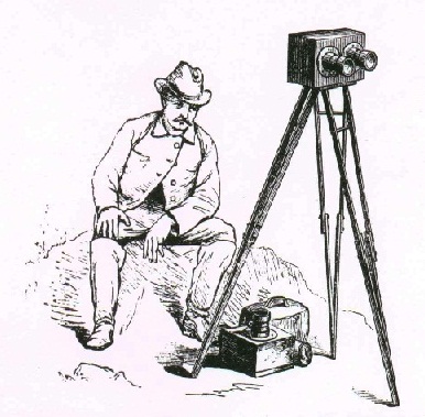 Mid-1800s man in period dress seated next to an early camera on a tripod.