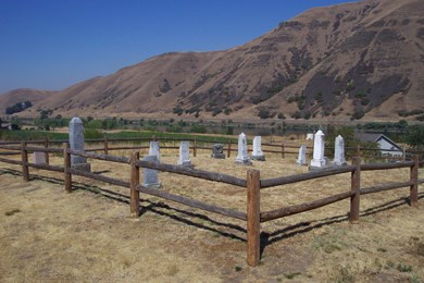 A fenced in cemetery with eleven headstones and the mountains in the background.