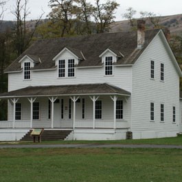 A white two story house with a porch and a wayside in front.