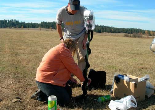 A man and a women conducting soil monitoring in a grassy field.