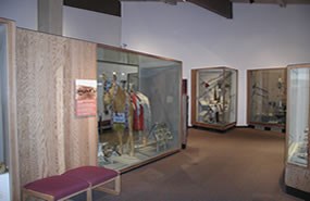 A room with museum exhibits and display cases filled with traditional Nez Perce clothing, tools, weapons, and ceremonial objects.