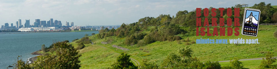 Lush vegetation on the top of Spectacle Island's North drumlin dominates the foreground. Boston's skyline can be seen in the distance.  The park's logo with tag line minutes away, worlds apart empashises the stark contrast between the city and islands. 