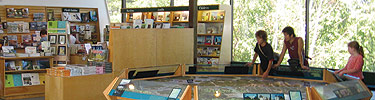 Three visitors explore the 3-D map of the island at the visitor center. Books are on display in the sales area.