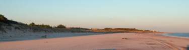 Golden glow of sunset on an empty beach, with the shadow of the dunes seeming to grow.