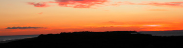 Red-orange sky, mottled with wispy pink and purple clouds, over the dark, low profile of Fire Island.