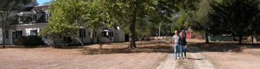 Couple strolls down shaded trail past historic house.