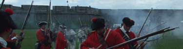 bright white smoke surrounds dark greens and reds as british reenactors display the weaponry tactics of the day