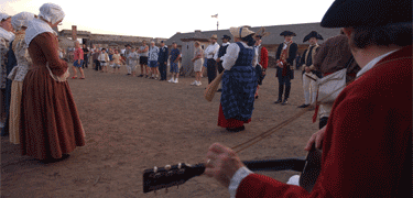 a guitar, beyond people of all sizes stand in a dusty line ready to dance