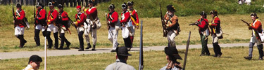 British soldiers, red coats as bright as blood, walk in line loading muskets preparing to fire at the fort for a demonstration
