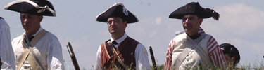 3 men with black cocked hats stand in a row. there is blue sky behind. they where white clothes