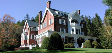 Three story brick mansion with wide porch, white trim, tall chimneys, shrubs and green lawn. Photo by Jack Boucher.
