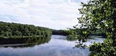 The blue sky is reflected as it flows between thickly wooded banks.