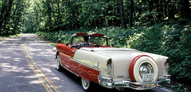 A red and white 1955 convertible enters a spectacular tree tunnel on Skyline Drive.