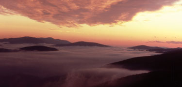 A yellow and orange sky meets islands of mountains in a fog ocean.