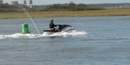 PWC passes a green channel marker in bay near wooded shoreline and salt marsh.