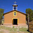 A pinkish-brown adobe chapel stands against the deep blue New Mexican sky.
