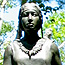 A bronze statue of a Passamaquoddy woman is surrounded by trees.