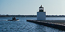On a sunny day, a small boat motors past the 1871 lighthouse at the tip of Derby Wharf.