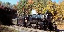 A steam locomotive exits a tunnel and rolls past fall colors on one of Steamtown's long train rides.