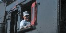 An engineer peers out of the cab of a steam locomotive.  The engineer drives the train, but the conductor is in charge.